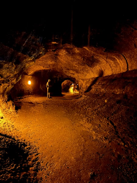 Illuminated lava tube cave passage with visitors exploring the golden-lit volcanic rock formations underground. — Hawaiʻi Volcanoes National Park, Big Island, Hawaii