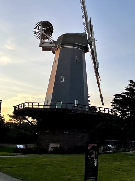 Historic Dutch windmill with brick tower and rotating sails viewed from ground level at dusk in San Francisco. — Golden Gate Park, San Francisco