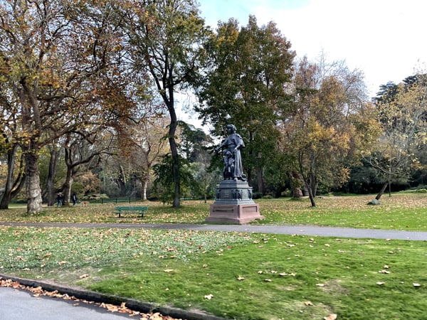 A bronze statue monument stands in a tree-lined park during autumn with fallen leaves on the grass. — Golden Gate Park, San Francisco
