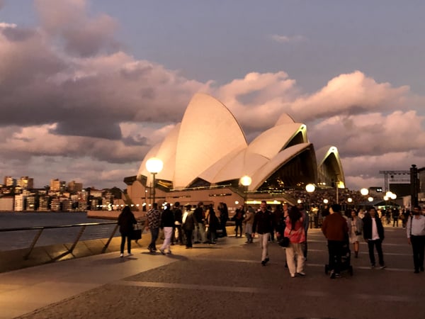 Sydney Opera House illuminated at dusk with crowds gathered on the forecourt and harbor visible to the left. — Sydney Opera House, Sydney