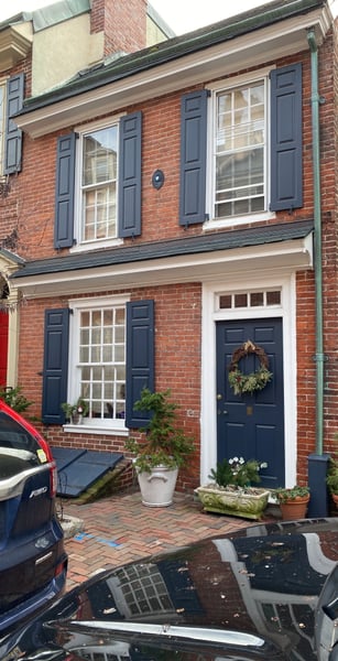 Historic red brick rowhouse facade with navy shutters, white trim windows, and festive wreath on door at street level. — South Philadelphia, Philadelphia