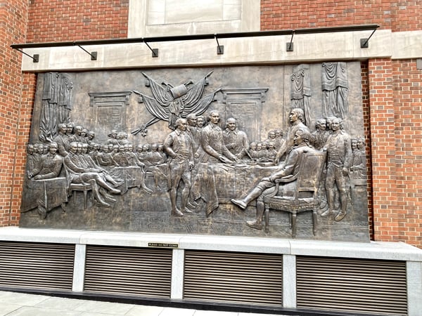 Large bronze relief sculpture depicting a historical gathering with figures in 18th-century dress, mounted on a brick… — Museum of the American Revolution, Philadelphia