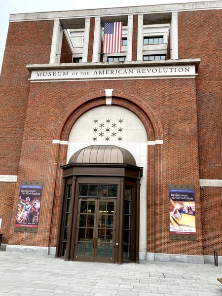 Facade of the Museum of the American Revolution, a brick and stone building with classical arched entrance and American… — Museum of the American Revolution, Philadelphia