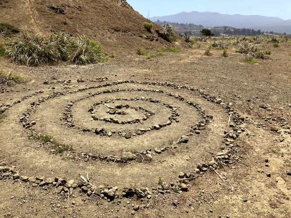 Spiral rock arrangement on a hillside overlooking a valley with mountains in the distance. — San Francisco