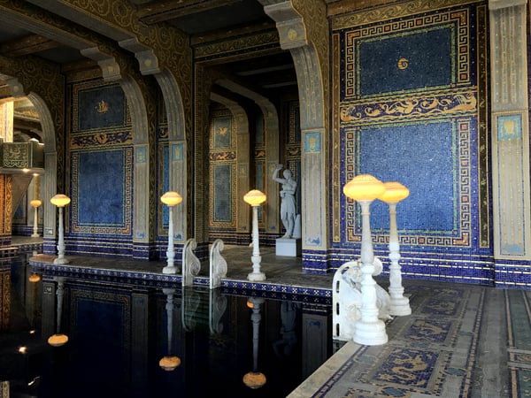 Classical Roman bath interior with blue mosaic walls, ornate columns, and sculptural details illuminated by mushroom… — Hearst Castle, Big Sur & the Highway 1 Coast
