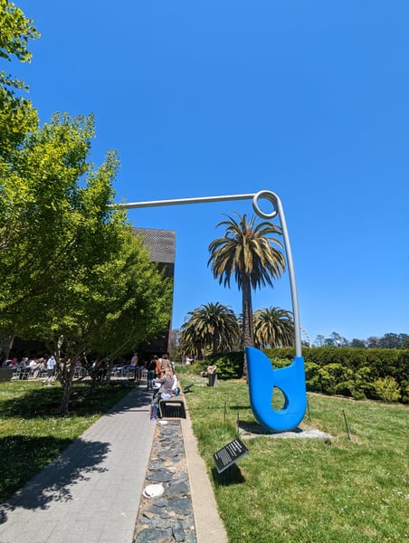 Giant Safety Pin sculpture in a San Francisco park with palm trees and manicured gardens under clear blue sky. — Inner Sunset, San Francisco