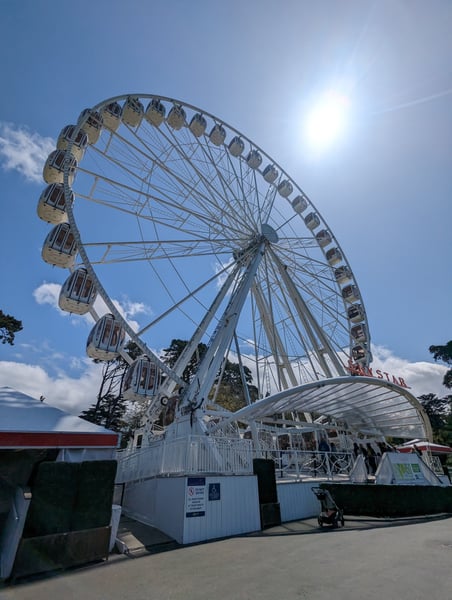 A large Ferris wheel with cream-colored gondolas photographed from ground level against a blue sky with light clouds. — Inner Sunset, San Francisco