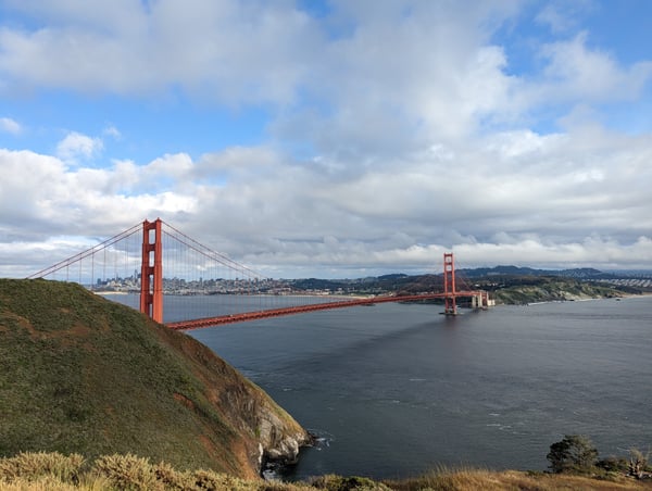 Golden Gate Bridge viewed from a coastal overlook with San Francisco skyline in the background.