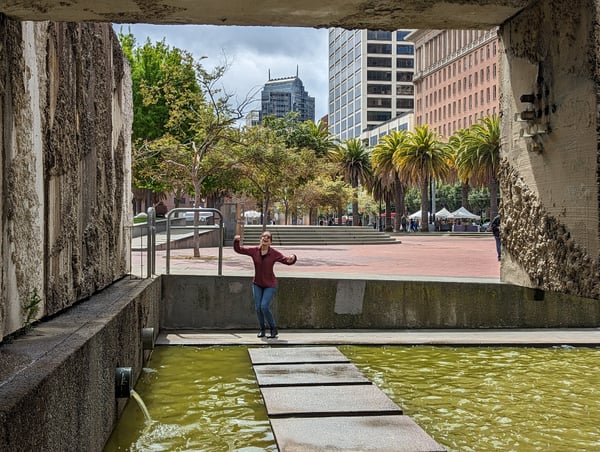 Person enjoying a modern urban plaza framed through a concrete underpass, with downtown buildings and palm trees… — Financial District, San Francisco