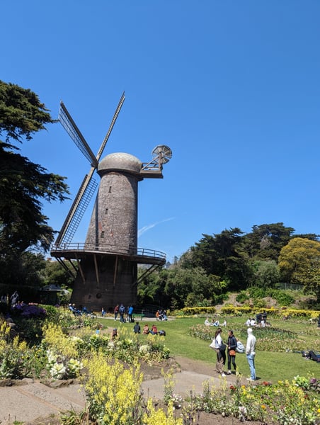 Historic Dutch windmill with brick tower in Queen Wilhelmina Tulip Garden, surrounded by flowering gardens and visitors… — Outer Richmond, San Francisco