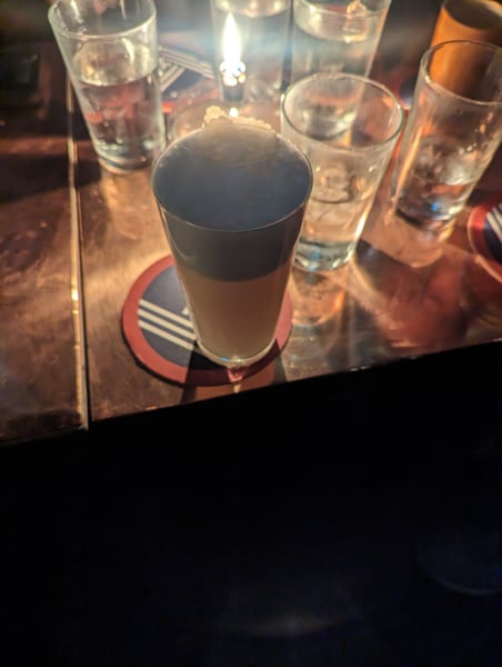 A beer glass with dark top and light base sits on a coaster surrounded by water glasses at a bar table in Paris. — 3rd Arrondissement, Paris