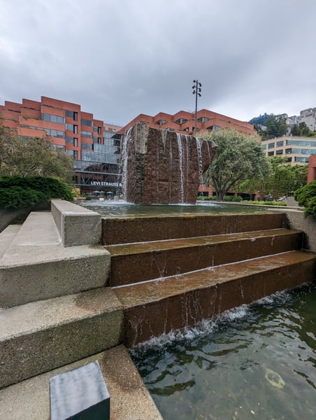Modern sculptural fountain with water cascading down a textured stone monolith in an urban plaza surrounded by… — Financial District, San Francisco