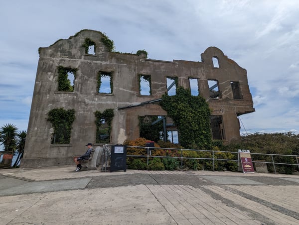 Alcatraz Main Cell House ruins with ivy-covered concrete walls and empty window frames viewed from the ground level… — Alcatraz Main Cell House, San Francisco