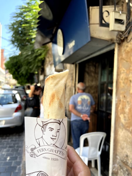Fresh flatbread from Fern Ghattas bakery held in hand on a street in Beirut, with the historic storefront visible in…