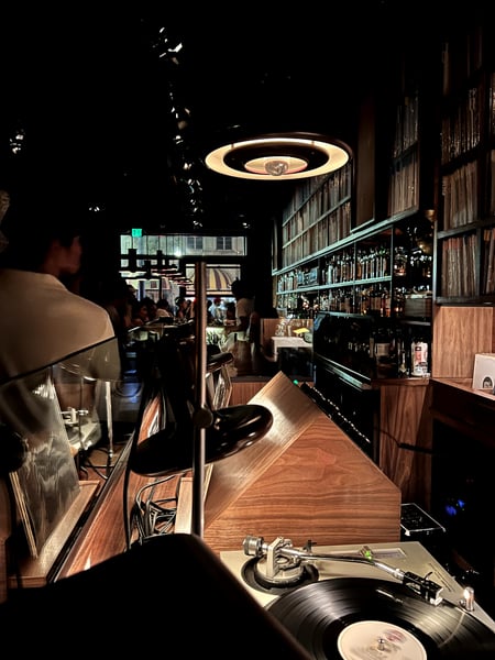 Interior of a nightclub or music venue with turntable, illuminated circular ceiling fixture, bar counter, and bottles… — Los Angeles