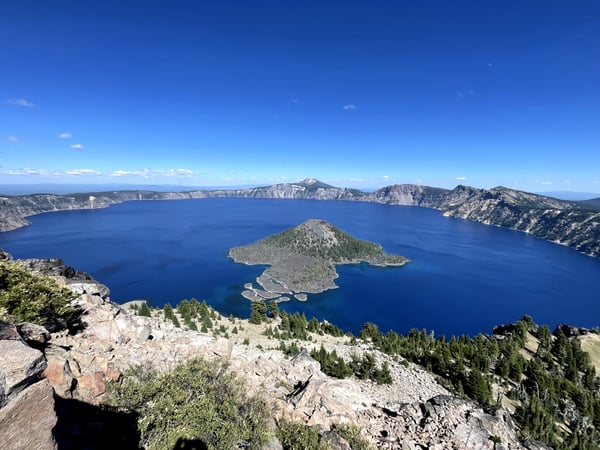 Deep blue alpine lake with forested island and caldera rim viewed from rocky overlook at Crater Lake, Oregon. — Crater Lake National Park