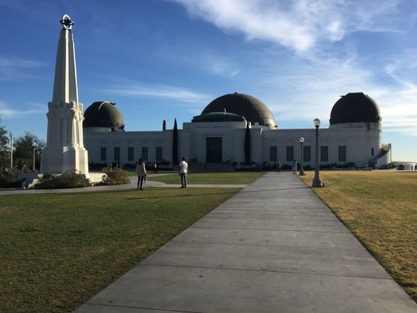 Griffith Observatory's white neoclassical building with three domes viewed from the main approach pathway on a clear… — Los Angeles