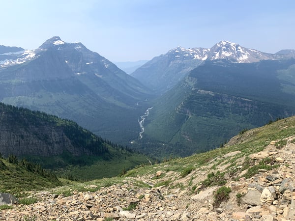 Alpine valley with snow-capped peaks and a winding river viewed from a high trail overlook in Glacier National Park.
