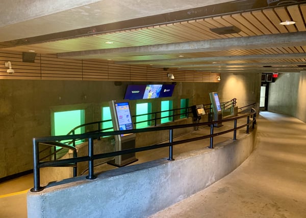 Modern underground transit corridor with curved concrete walls, metal railings, illuminated green panels, and digital… — Seattle
