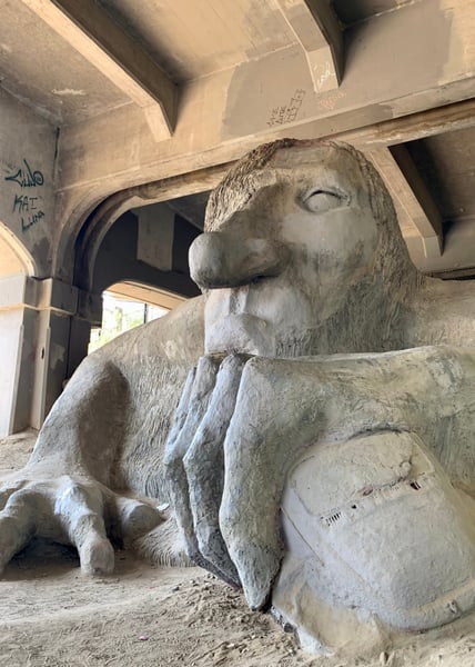 Stone sculpture of a turtle with distinctive carved features displayed indoors beneath concrete structural beams. — Fremont Troll, Seattle