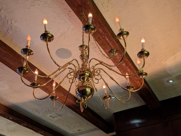 Ornate brass chandelier with lit candle-style bulbs mounted on textured ceiling with exposed wooden beam. — Los Angeles