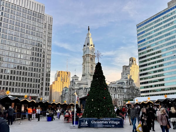 Christmas Village market in Philadelphia with decorated tree, vendor stalls, and City Hall clock tower in background. — Center City, Philadelphia