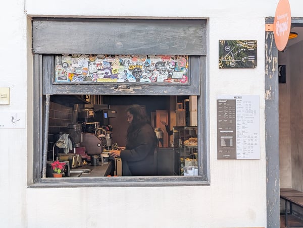 Barista working at Almanegra Café counter viewed through street-level storefront window in Mexico City.