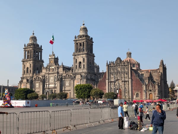 Metropolitan Cathedral of Mexico City viewed from the Zócalo plaza, with the Mexican flag visible and crowds gathered…