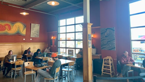 Interior of a modern café in Portland with colorful walls, large windows, wooden furniture, and patrons working on… — Buckman, Portland