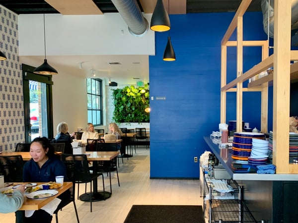 Modern café interior with diners, featuring bold blue accent wall, hanging pendant lights, and a living plant… — Buckman, Portland