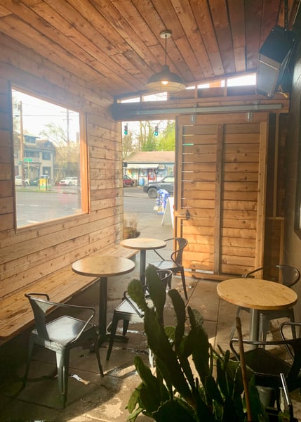Interior of a wooden-walled café with round tables and chairs, viewed from inside looking toward the street-facing… — Buckman, Portland