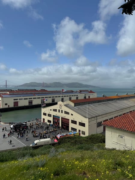 Maritime building and pier at waterfront with Golden Gate Bridge visible across the bay, viewed from elevated grassy… — Fort Mason, San Francisco