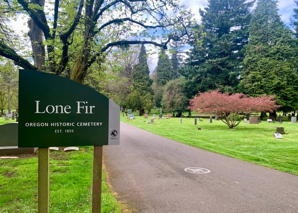 Entrance sign to Lone Fir Oregon Historic Cemetery, established 1855, with tree-lined grounds and headstones visible. — Central Eastside, Portland