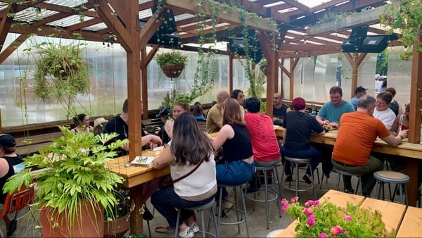 Indoor greenhouse café with wooden pergola, hanging plants, and patrons seated at communal tables. — Hosford-Abernethy, Portland