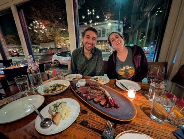 Two diners enjoying a meal at an upscale restaurant with night city views through floor-to-ceiling windows in Seattle.