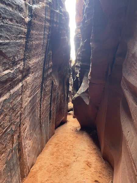 Narrow slot canyon with towering red rock walls and sandy floor, lit by sky opening above. — The Wave Trail, Kanab & The Wave