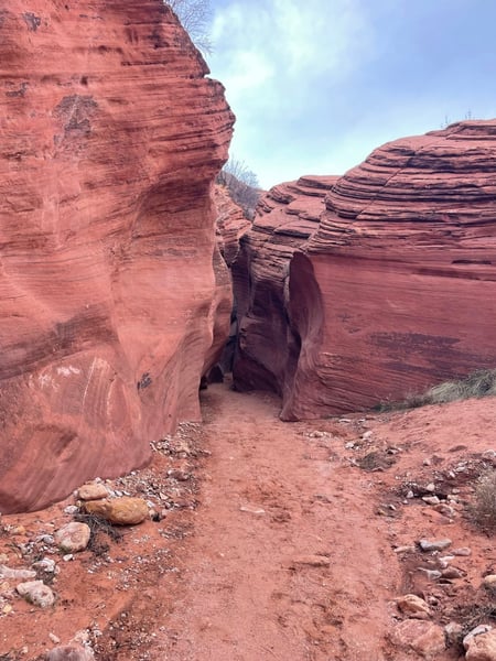 Narrow red sandstone canyon passage with layered rock formations viewed from ground level on a hiking trail. — Kanab & The Wave