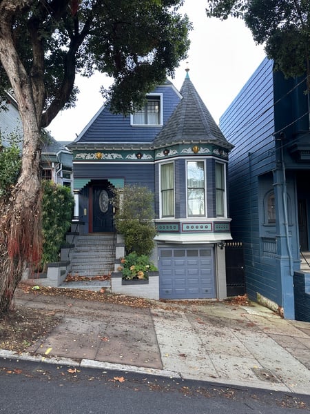 Victorian-style house with distinctive turret and blue siding on a San Francisco street, photographed from the sidewalk. — Haight-Ashbury, San Francisco