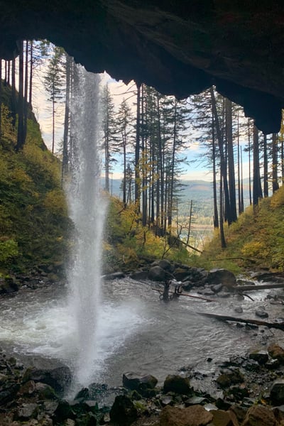 A waterfall cascades through a forested canyon with coniferous trees and mountain valley views visible in the distance. — Mount Hood National Forest, Columbia River Gorge
