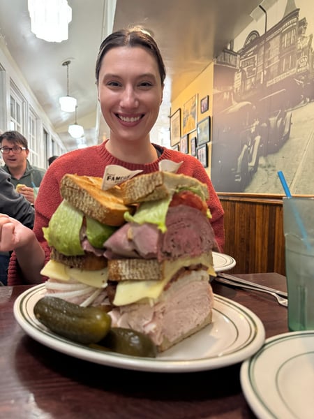 Woman holding a stacked deli sandwich with roast beef, cheese, and pickles in a Philadelphia restaurant interior. — Center City, Philadelphia