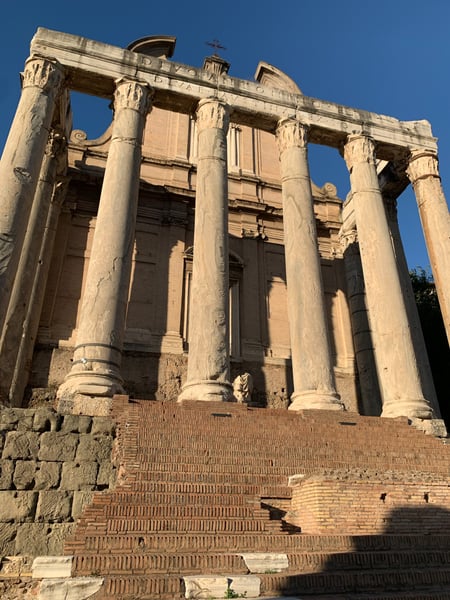 Roman temple with Corinthian columns and brick staircase viewed from ground level against clear blue sky. — Campitelli, Rome