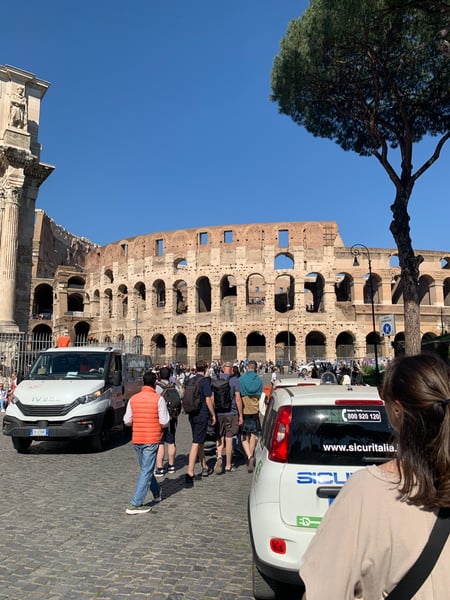 Colosseum viewed from the plaza below, with visitors and security vehicles present on a clear day. — Campitelli, Rome