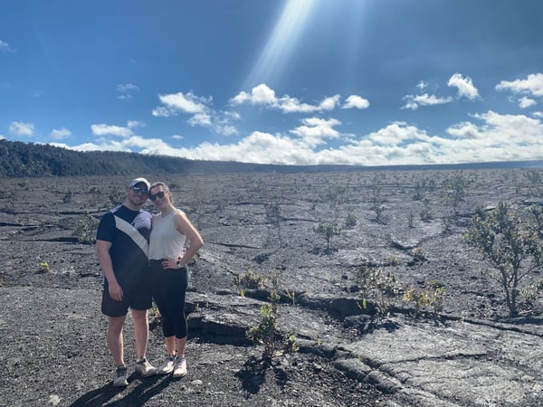 Two visitors pose in Hawaii Volcanoes National Park on an expansive lava field with recovering vegetation and forested… — Hawaiʻi Volcanoes National Park, Big Island, Hawaii